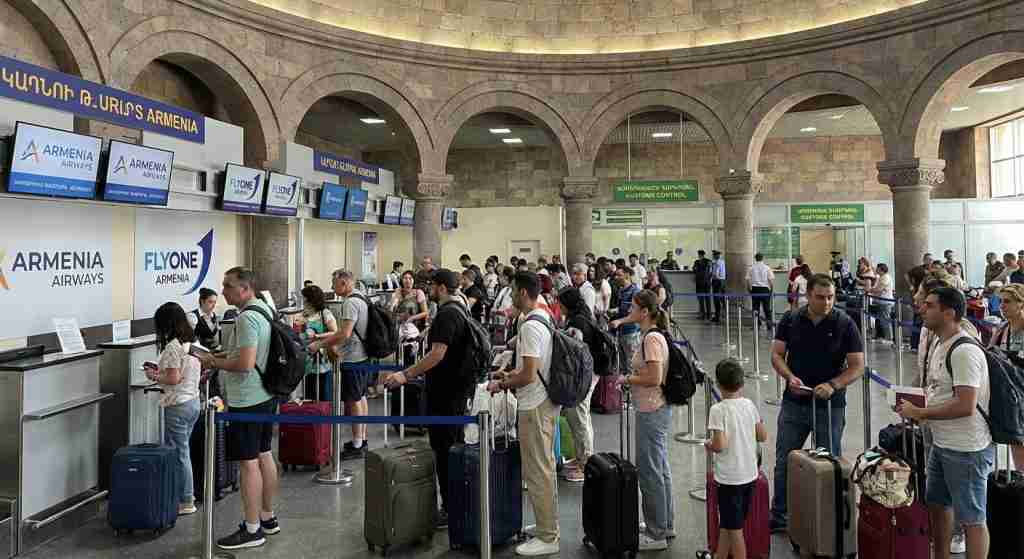 A busy airport terminal with travelers at check-in counters surrounded by Armenian architecture.
