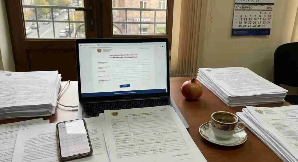A workspace with a laptop showing a tax residency application, papers, and a smartphone.