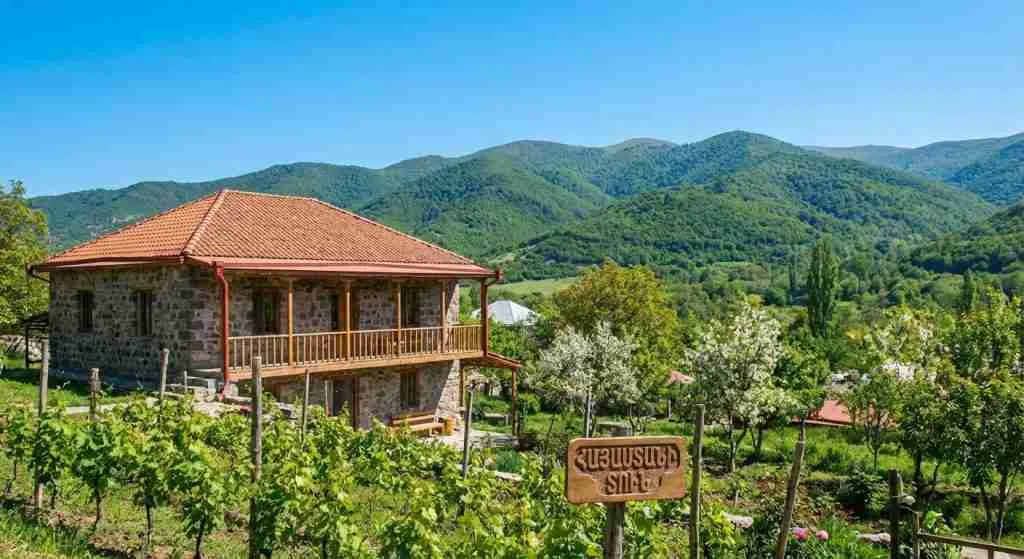 A traditional Armenian house surrounded by mountains under a clear sky.