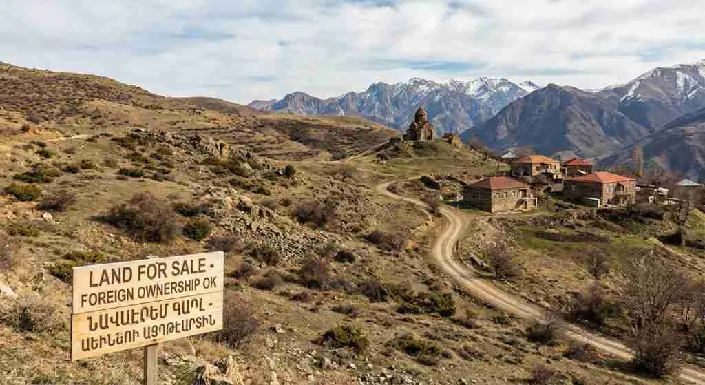Scenic view of rural Armenia with mountains and typical local buildings, representing non-agricultural lands available for purchase.