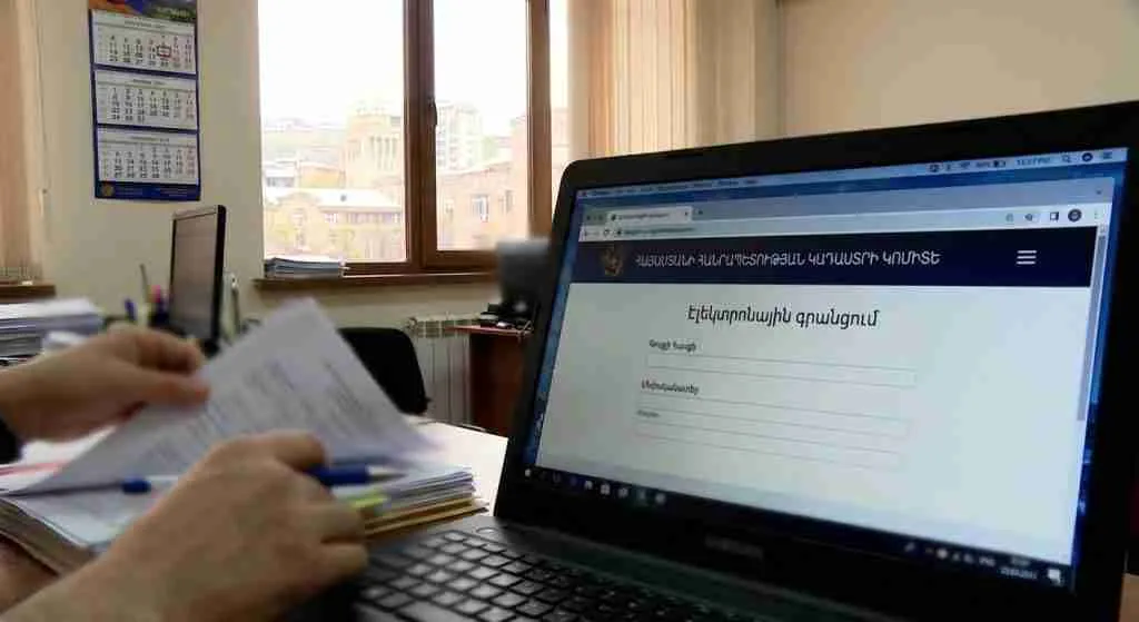 一台笔记本电脑屏幕上显示着房产登记门户网站,画面中有双手在整理文件。