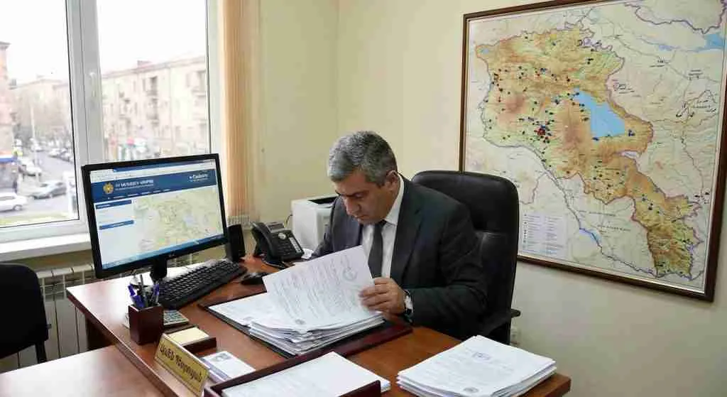 An office desk with property documents and a computer screen displaying a real estate registration portal in Armenia.