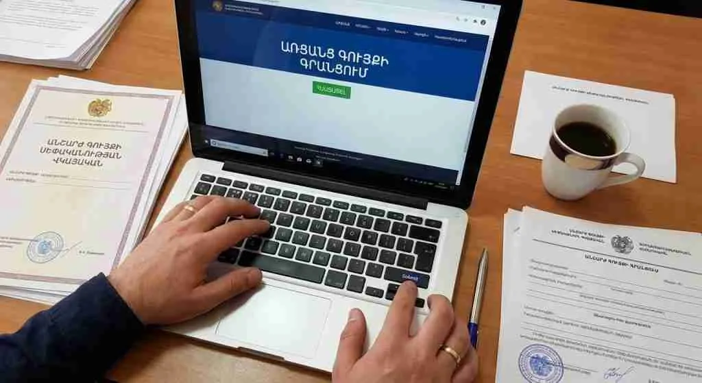 Hands typing on a laptop with property documents nearby in an Armenian office setting.
