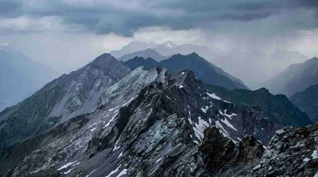 Layered mountain ridges fade into storm haze under a dusk sky, nearest peak sharp against soft distant layers