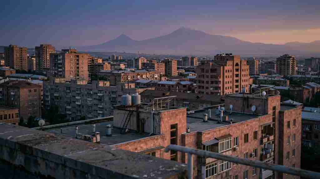Տուֆե քարե և բետոնե շենքերի շերտավոր տանիքներ Երևանում՝ մթնշաղին, մշուշոտ լեռներով։